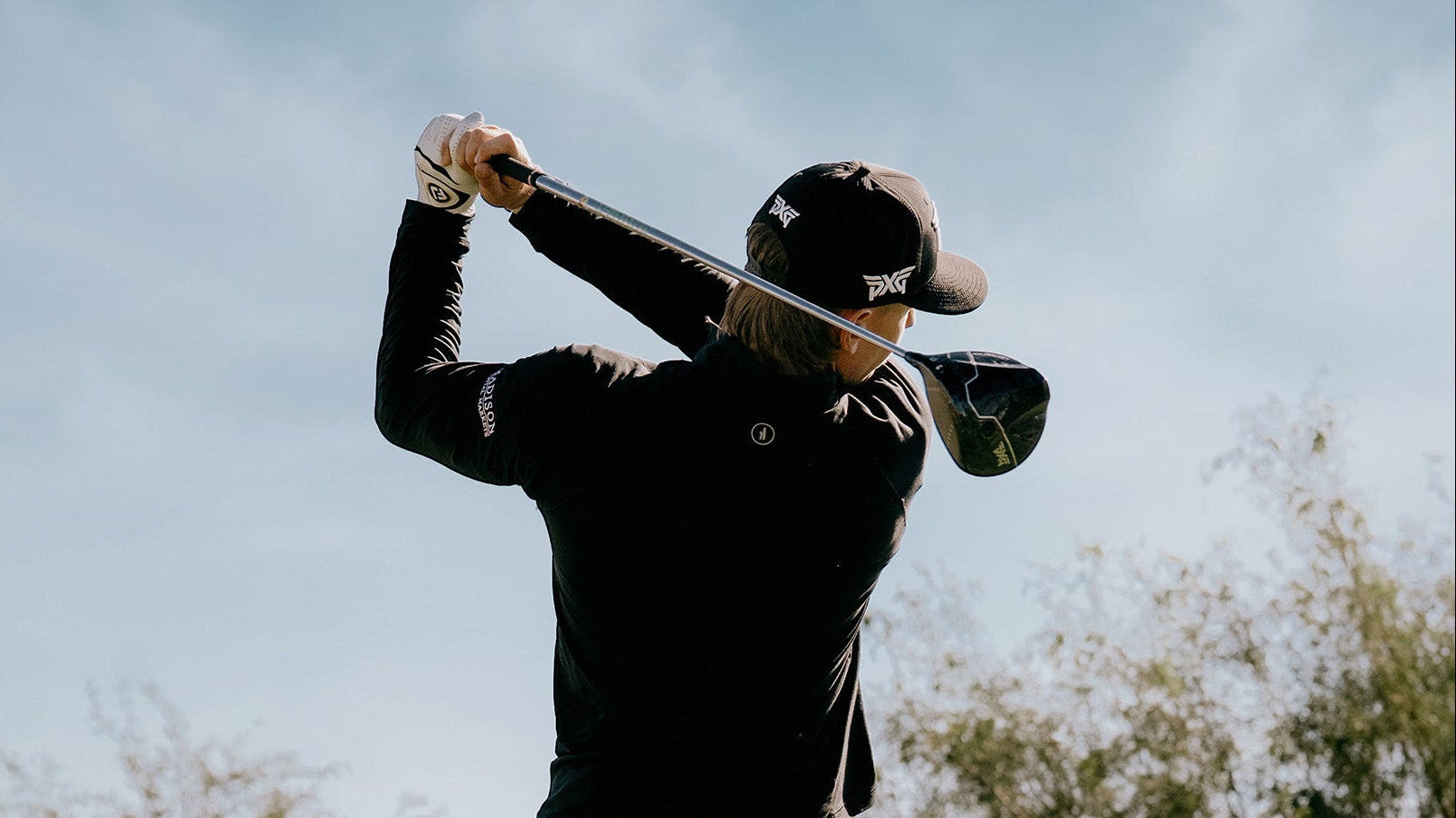 Person playing golf with a club, wearing a black outfit and cap.