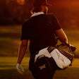 A golfer seen from behind on a golf course at sunset, carrying a white and black golf bag with a visible 
PXG logo.